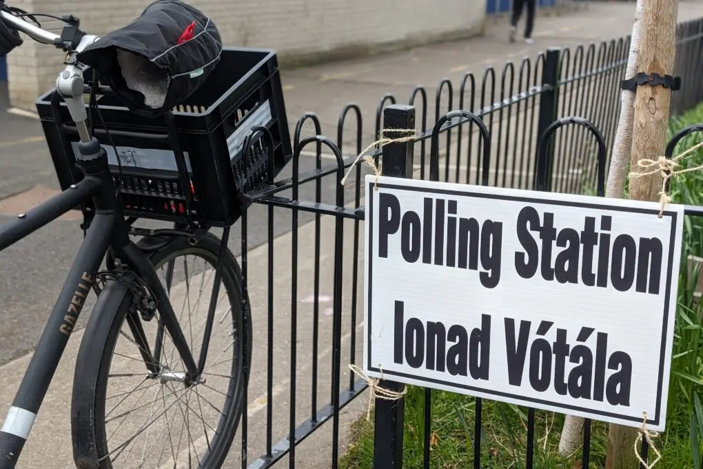 Polling Station sign hung on a black metal fence, with a black Dutch style bicycle beside